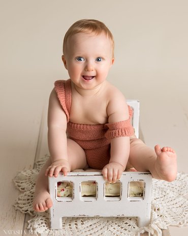 ett årig baby sitter på docksäng och poserar på babyfotografering